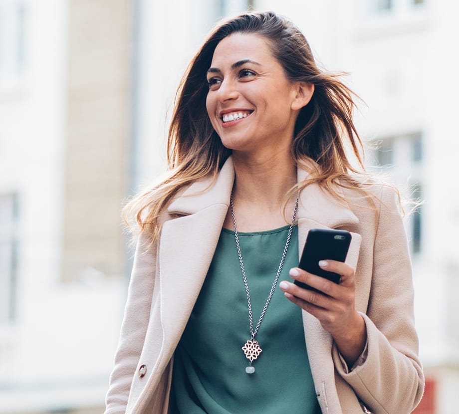 Woman smiling while holding phone, wearing green shirt and beige coat